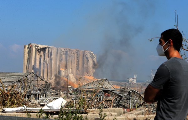 A man wearing a protective mask against the coronavirus stands across the road from the damaged grain silos of Beirut's harbour on August 5th, one day after a powerful twin explosion tore through Lebanon's capital. [STR/AFP]