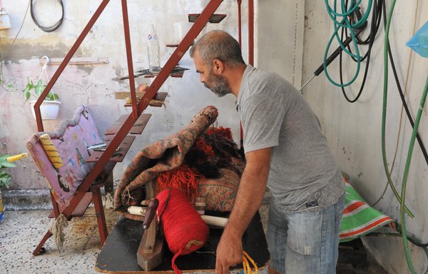 Syrian refugee Abdel Wahab Shami learned the craft of carpet repair and restoration, and turned a section of the roof of the room that shelters his family into a workshop where he mends carpets. [Ziad Hatem]