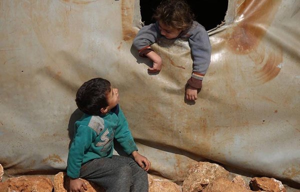 طفل سوري يتحدث إلى طفل آخر من داخل خيمة بمخيم للنازحين. [علي حاج سليمان]