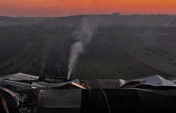 Smoke rises from a tent at al-Tah camp. Hundreds of families displaced from their villages face difficult conditions in rural Idlib, with their tents in need of repair and heating materials. Many rely on firewood for heating. [Abdul Salam al-Youssef]