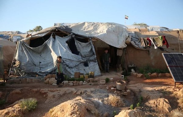 Children play in front of their torn tent in al-Tah camp in Syria's Idlib province, where conditions are harsh. [Abdul Salam Youssef]
